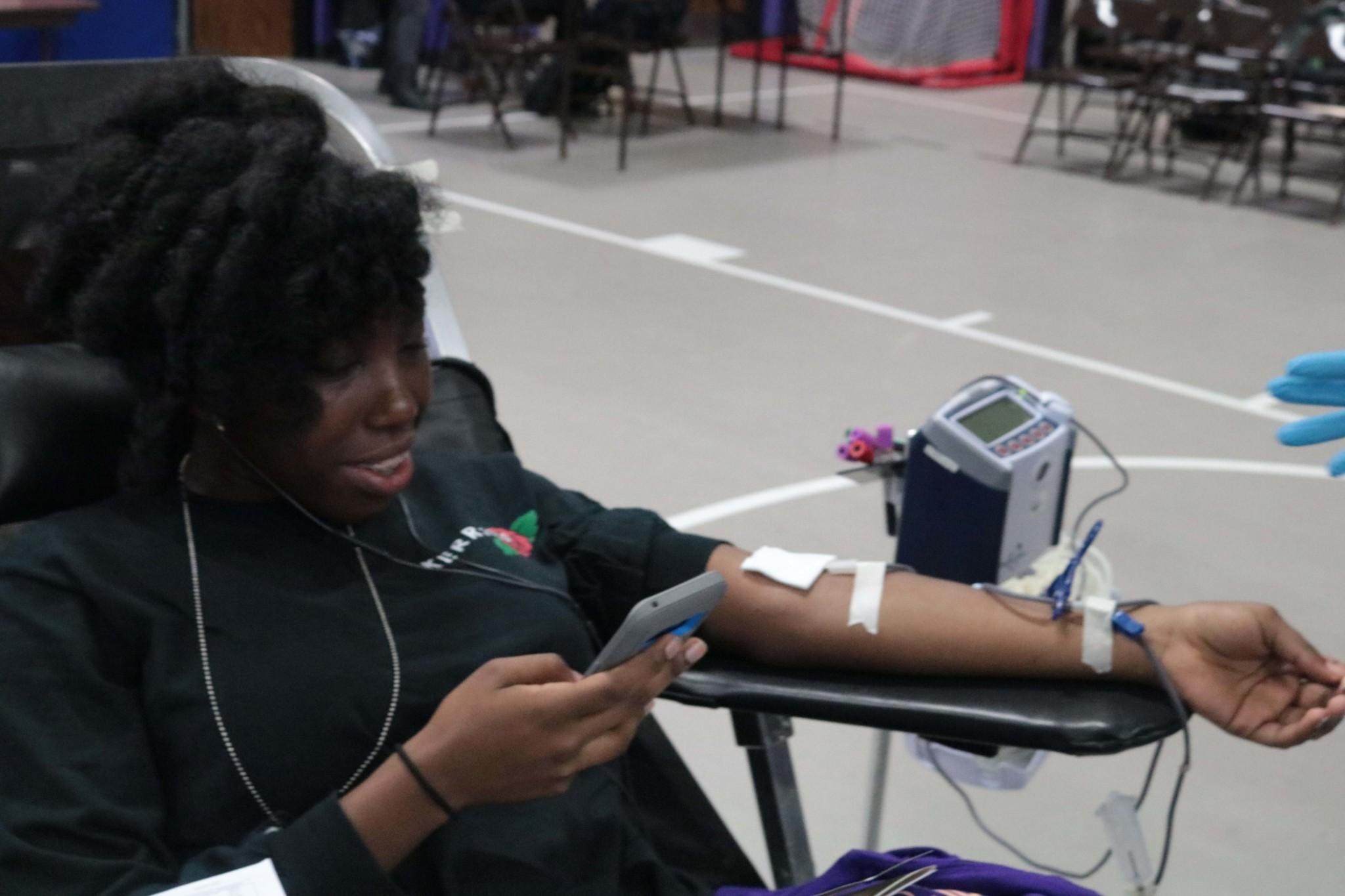 Dominique Carter, a junior, is getting her blood drawn while on her phone.