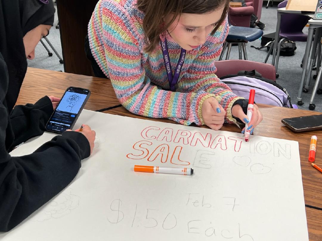 The Perfect Bloom: Seniors Rebecca Draper and Urooj Hashmi make a poster for carnation sales. They worked after-school to add logistical information. "It was fun drawing the carnation flowers," Draper said.