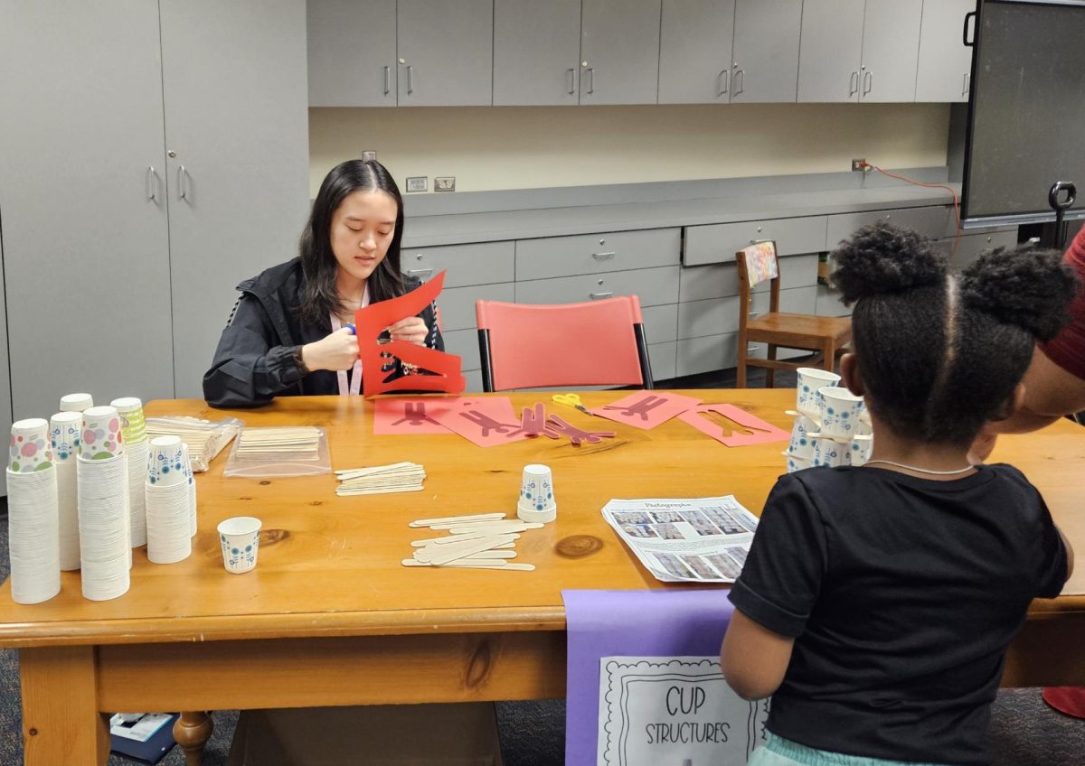 Connecting With Younger Generation: Senior Jenny Nguyen cuts prints outs for zipline activity. She is in charge of the tower building station, where cups and popsicle sticks are given to students to build the towers. "It was fun seeing how the kids were competing to build the tallest tower," Nguyen said. 