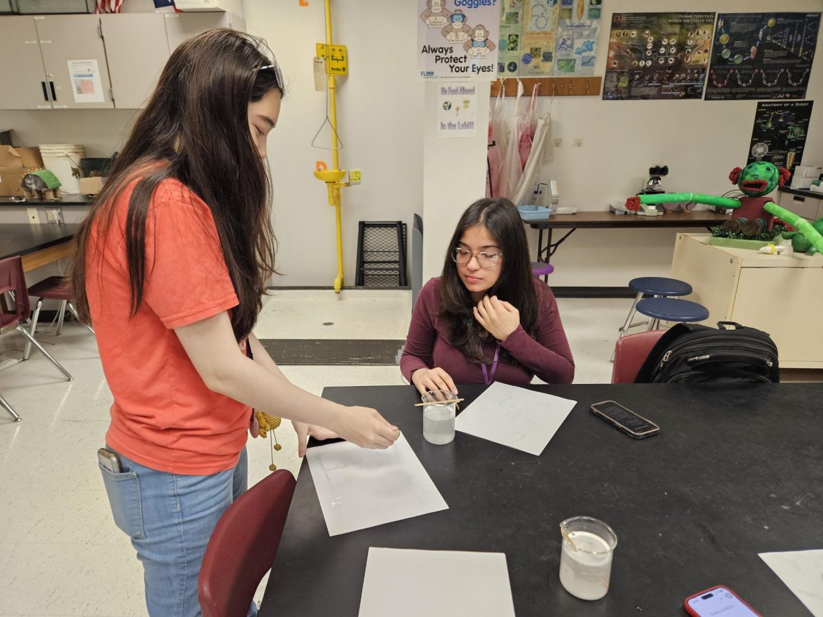 The Finale: President Iris Hoang-Dugan conducts experiment with club member Maria Bongah. She dips her paint brush in a mixture of baking soda and water to write on the piece of paper without it showing. "It was fun looking at the final pieces," Hoang-Dugan said. 